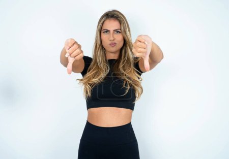 Photo for Young caucasian woman wearing sports clothes  being upset showing thumb down with two hands. Dislike concept. - Royalty Free Image