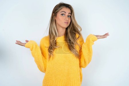 Téléchargez les photos : Jeune femme caucasienne attrayante négligente portant un pull jaune haussant les épaules, oups. - en image libre de droit