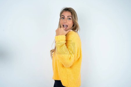 Téléchargez les photos : Impressionné jeune femme caucasienne portant point pull jaune de retour à l'espace vide - en image libre de droit