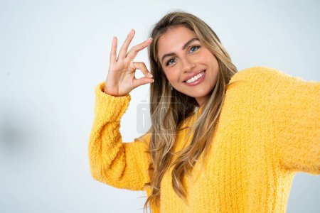 Téléchargez les photos : Portrait de jolie jeune femme caucasienne gaie portant un pull jaune faisant selfie montrant le symbole d'okey - en image libre de droit