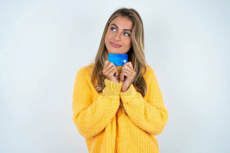 Téléchargez les photos : Photo de joyeux jeune femme caucasienne portant pull jaune tenant carte de débit regarder espace vide - en image libre de droit