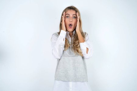 Photo for Caucasian woman wearing white shirt with scared expression, keeps hands on head, jaw dropped, has terrific expression. Omg concept - Royalty Free Image