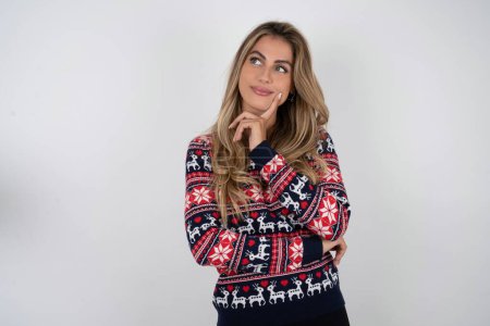 Téléchargez les photos : Femme caucasienne réfléchie portant chandail de Noël tient menton et regarde loin fait pénalement grand plan - en image libre de droit