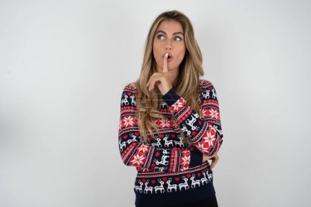 Photo for Caucasian woman wearing christmas sweater silence gesture keeps index finger to lips makes hush sign. Asks not to share secret - Royalty Free Image