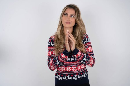 Photo for Caucasian woman wearing christmas sweater steepled fingers and looks mysterious aside has great evil plan in mind - Royalty Free Image