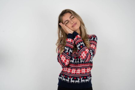 Photo for Caucasian woman wearing christmas sweater leans on pressed palms closes eyes and has pleasant smile dreams about something - Royalty Free Image