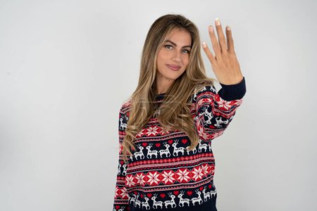 Téléchargez les photos : Femme caucasienne portant chandail de Noël souriant et regardant amical, montrant numéro quatre ou quatrième avec la main vers l'avant, compte à rebours - en image libre de droit
