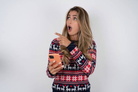 Téléchargez les photos : Femme caucasienne étourdie portant des points de pull de Noël sur le côté droit espace de copie, recommande le produit, voit chose étonnante - en image libre de droit