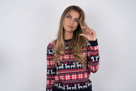 Photo for Displeased caucasian woman wearing christmas sweater shapes little hand sign demonstrates something not very big. Body language concept. - Royalty Free Image