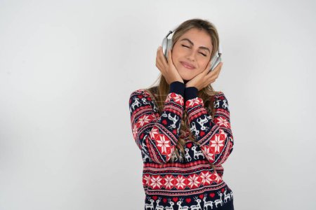 Téléchargez les photos : Femme caucasienne agréable portant chandail de Noël aime écouter mélodie agréable garde les mains sur casque stéréo ferme les yeux. Passer du temps libre avec la musique - en image libre de droit
