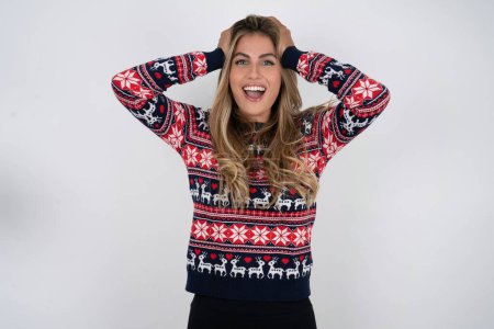 Photo for Cheerful overjoyed caucasian woman wearing christmas sweater reacts rising hands over head after receiving great news. - Royalty Free Image