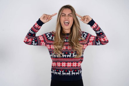 Foto de Foto de mujer caucásica loca usando suéter de Navidad gritando y señalando con los dedos a los ojos cerrados pelo - Imagen libre de derechos