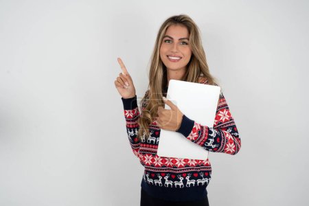 Photo for Caucasian woman wearing christmas sweater holding laptop showing copy empty space ad - Royalty Free Image