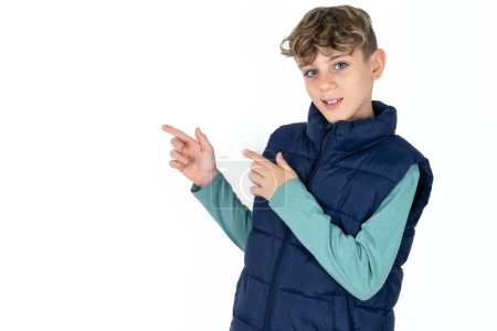 Foto de Guapo caucásico adolescente chico en blanco estudio fondo indicando dedo vacío espacio mostrando mejores precios bajos, mirando a la cámara - Imagen libre de derechos