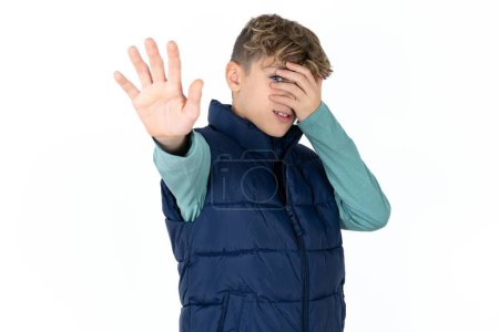 Photo for Handsome caucasian teenager boy on white studio background covers eyes with palm and doing stop gesture, tries to hide from everybody. - Royalty Free Image