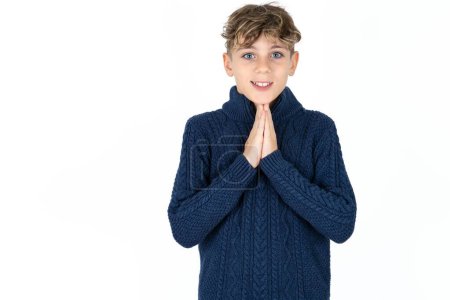 Foto de Guapo caucásico adolescente chico en blanco estudio fondo orando con las manos juntas pidiendo perdón sonriendo confiado. - Imagen libre de derechos