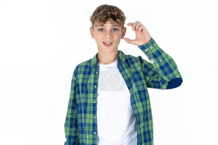 Téléchargez les photos : Beau garçon adolescent caucasien sur fond blanc studio geste souriant et confiant avec la main faisant signe de petite taille avec les doigts à la recherche et la caméra. Concept de mesure - en image libre de droit