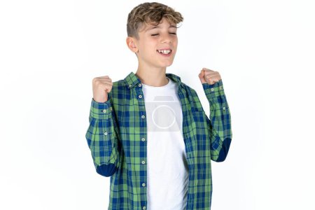 Ecstatic handsome caucasian teenager boy on white studio background shout loud yeah fist up raise win lottery