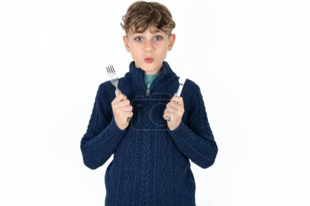 Téléchargez les photos : Affamé beau garçon adolescent caucasien sur fond blanc studio tenant dans la main couteau fourchette veulent savoureux délicieux pizza tarte - en image libre de droit