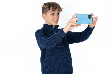 Foto de Guapo caucásico adolescente chico en blanco estudio fondo tomar un selfie para publicar en las redes sociales o tener una videollamada con amigos. - Imagen libre de derechos