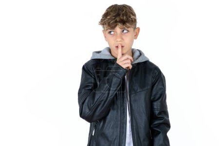 Téléchargez les photos : Beau garçon adolescent caucasien sur fond blanc studio geste de silence garde index aux lèvres fait signe de silence. Demande de ne pas partager le secret - en image libre de droit