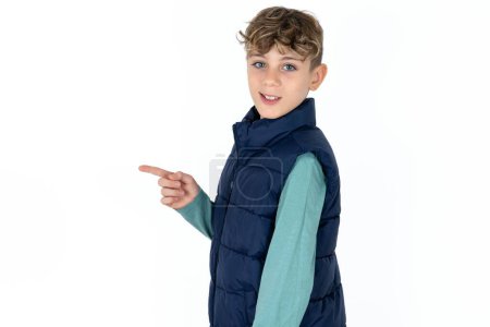 Téléchargez les photos : Photo de profil de beau garçon adolescent caucasien sur fond de studio blanc indiquer doigt vide offre d'espace - en image libre de droit