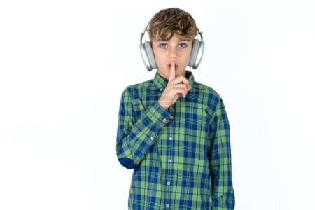 Photo for Handsome caucasian teenager boy on white studio background making hush gesture with finger on her lips wearing  wireless headphones. Be quiet. - Royalty Free Image