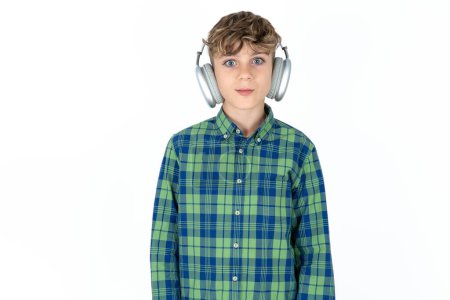 Photo for Serious displeased handsome caucasian teenager boy on white studio background looks puzzled at camera being angry wears stereo headphones listens music while walking at street - Royalty Free Image