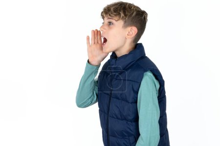 Foto de Guapo caucásico adolescente chico en blanco estudio fondo mirar vacío espacio sosteniendo la mano cara y gritando o llamando a alguien. - Imagen libre de derechos