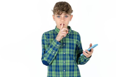 handsome caucasian teenager boy on white studio background holding modern gadget ask not tell secrets