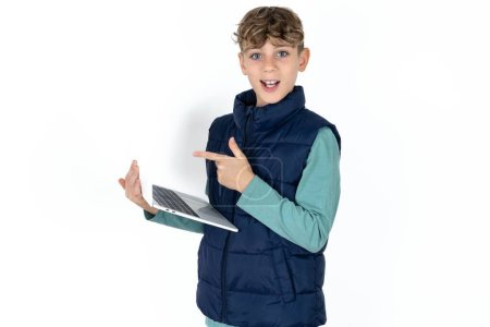 Photo for Shocked handsome caucasian teenager boy on white studio background pointing finger modern device - Royalty Free Image
