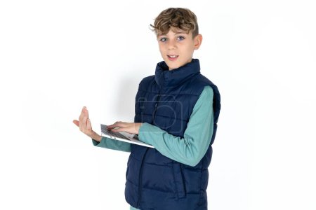 Téléchargez les photos : Adorable beau garçon adolescent caucasien sur fond de studio blanc tenant dispositif moderne - en image libre de droit
