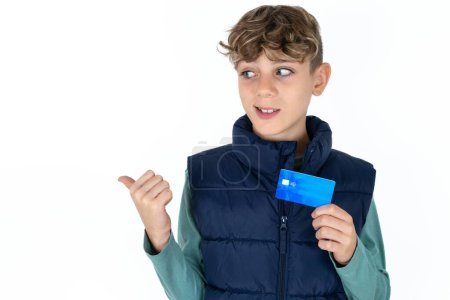 Foto de Guapo caucásico adolescente chico en blanco estudio fondo hold tarjeta de crédito punto vacío espacio - Imagen libre de derechos