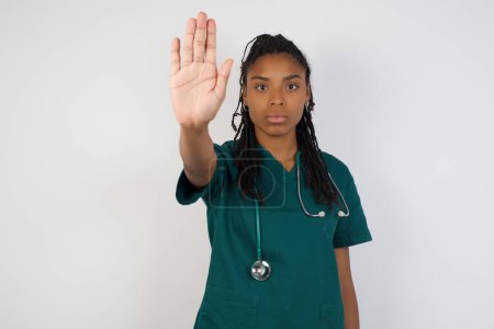 Téléchargez les photos : Jeune belle femme médecin afro-américaine faisant geste d'arrêt avec la paume de la main. Expression d'avertissement avec geste négatif et grave sur le visage isolé sur fond gris. - en image libre de droit
