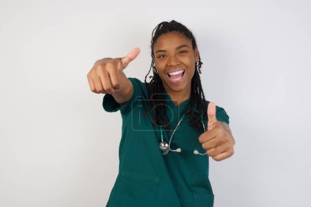 Téléchargez les photos : Jeune médecin femme sur fond isolé approuvant faire un geste positif avec la main, pouces levés souriant et heureux pour le succès. En regardant la caméra, geste gagnant. - en image libre de droit