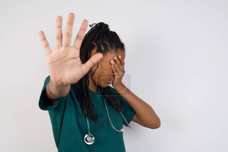 Photo for People, body language. Young african american doctor woman covers eyes with palm and doing stop gesture, tries to hide from everybody. Don't look at me, I don't want to see, feels ashamed or scared. - Royalty Free Image