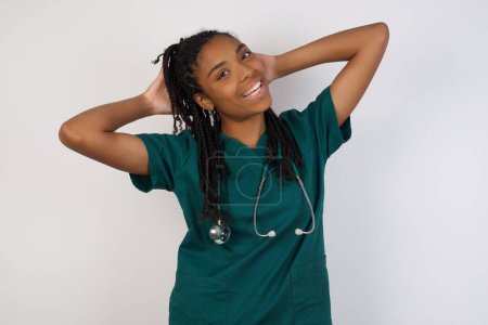Photo for Confidence and coquettish concept. Portrait of charming young doctor girl  wearing medical uniform, smiling broadly with self-assured expression while holding hands over her head. - Royalty Free Image
