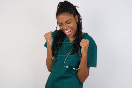 Téléchargez les photos : Médecin afro-américain se réjouissant de son succès et de la victoire serrant les poings avec joie. Femme chanceuse avec un chignon à cheveux heureux d'atteindre son objectif et ses objectifs. Émotions positives, sentiments. - en image libre de droit