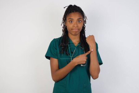 Téléchargez les photos : Belle jeune femme médecin afro-américaine sur fond isolé pressé de regarder le temps, impatience, bouleversé et en colère pour retard de délai - en image libre de droit