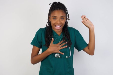 Téléchargez les photos : Promets-moi de ne pas regretter. Portrait d'heureuse femme médecin afro-américaine sincère levant un bras et tenant la main sur le cœur comme donner serment, promesse, dire la vérité, vous voulez croire, debout sur le fond - en image libre de droit