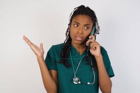 Photo for Young african american doctor woman talking on the phone over isolated background stressed with hand on face, shocked with shame and surprise face, angry and frustrated. Fear and upset for mistake. - Royalty Free Image