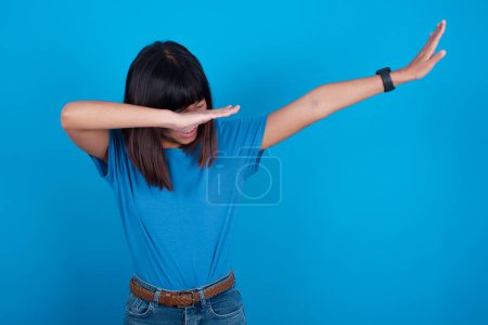 Téléchargez les photos : Photo de funky jeune femme asiatique portant t-shirt sur fond bleu montrer disco déplacer dab - en image libre de droit