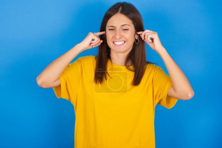 Photo for Happy beautiful young woman ignores loud music and plugs ears with fingers asks to turn off sound - Royalty Free Image