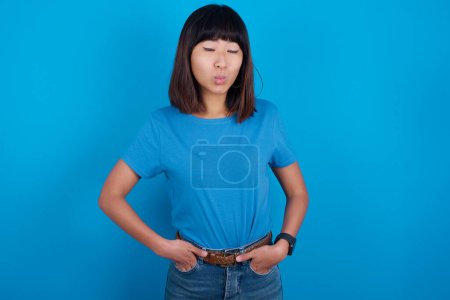 Téléchargez les photos : Portrait de belle jeune femme asiatique drôle portant t-shirt sur fond bleu envoyer baiser d'air - en image libre de droit
