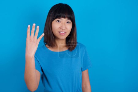 Photo for Young asian woman wearing t-shirt against blue background smiling and looking friendly, showing number four or fourth with hand forward, counting down - Royalty Free Image