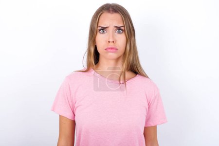 Young Caucasian girl wearing pink T-shirt on white background expressing disgust, unwillingness, disregard having tensive look frowning face, looking indignant with something.