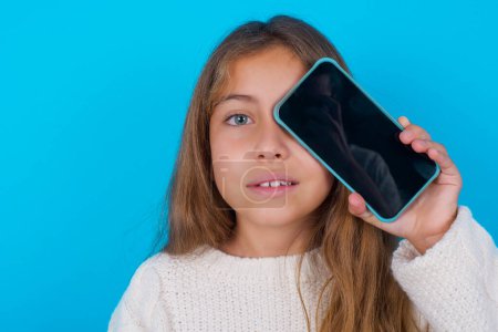 pretty teen girl holding modern smartphone covering one eye while smiling