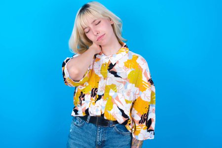 Photo for Caucasian girl wearing floral shirt isolated over blue background suffering from back and neck ache injury, touching neck with hand, muscular pain. - Royalty Free Image