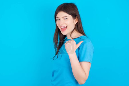Photo for Impressed young caucasian girl wearing blue T-shirt isolated over blue background  point back empty space - Royalty Free Image