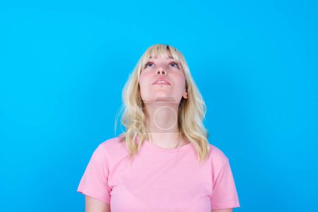 Foto de Caucásico chica usando rosa camiseta aislada sobre fondo azul mirando hacia arriba como él ve algo extraño. - Imagen libre de derechos